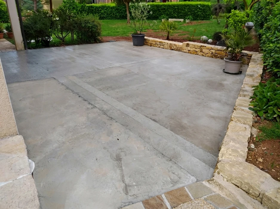 Terrasse extérieure en béton lissé avec joints de dilatation apparents, entourée d'un muret en pierres calcaires taillées