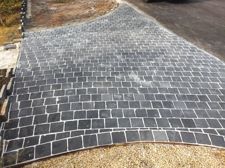 Allée extérieure pavée de pavés en pierre naturelle noire type basalte, format cubique irrégulier, joints blancs au mortier de ciment