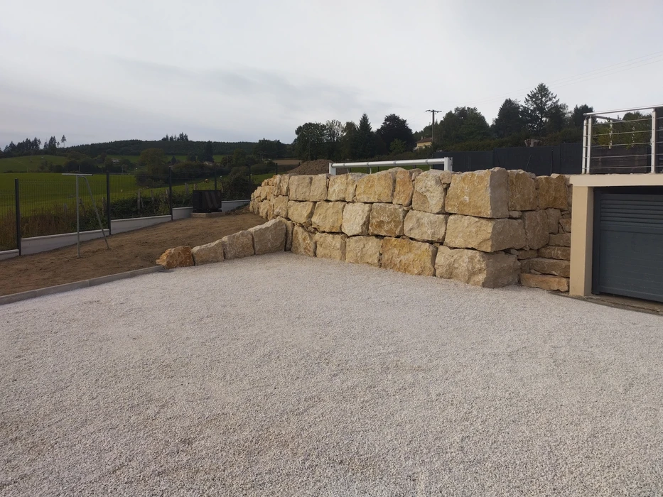 Mur de soutènement en grands blocs de calcaire beige-doré, disposés en assises horizontales irrégulières, retenant un remblai de terre