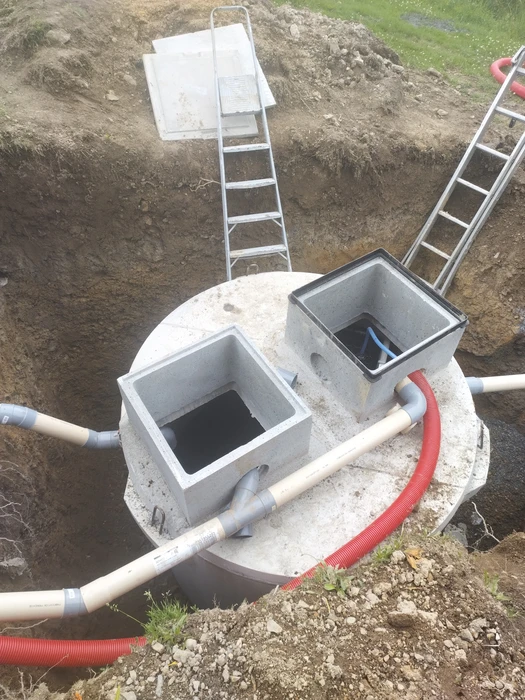 Chantier extérieur de pose d'une fosse septique en béton préfabriqué, partiellement enterrée