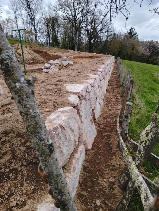 Mur de soutènement en cours de construction, en pierres de granite rose taillées, disposées en assises régulières sans mortier (mur en pierre sèche)