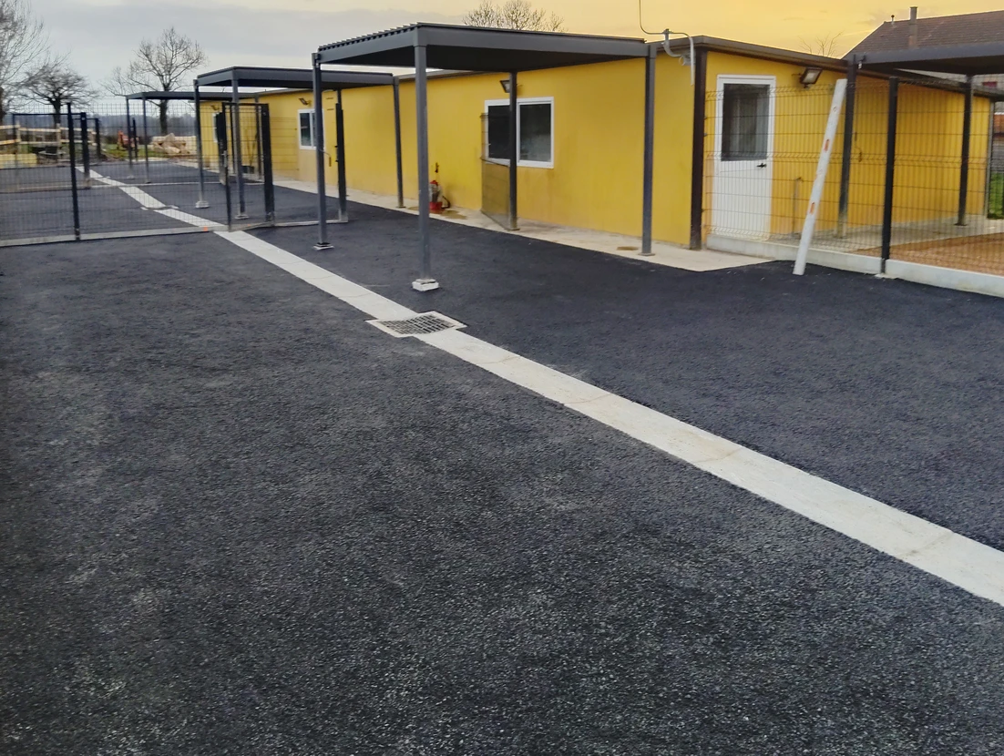 Parking fraîchement enrobé en enrobé bitumineux noir, délimité par des murets en béton et pierre