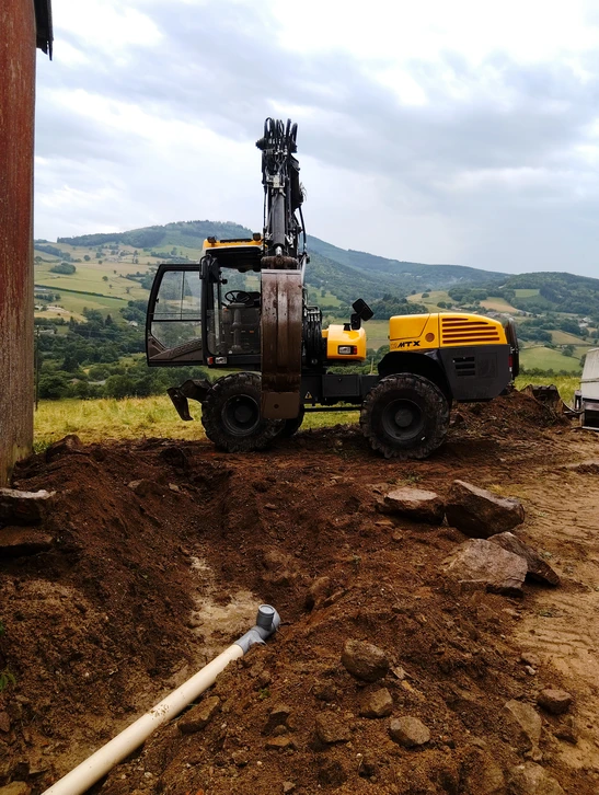 Chantier extérieur en pleine campagne avec pelleteuse hydraulique jaune sur chenilles en position de travail